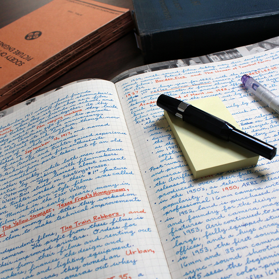 Image of notes in a notebook with books in the background and a pen and sticky notes on top.