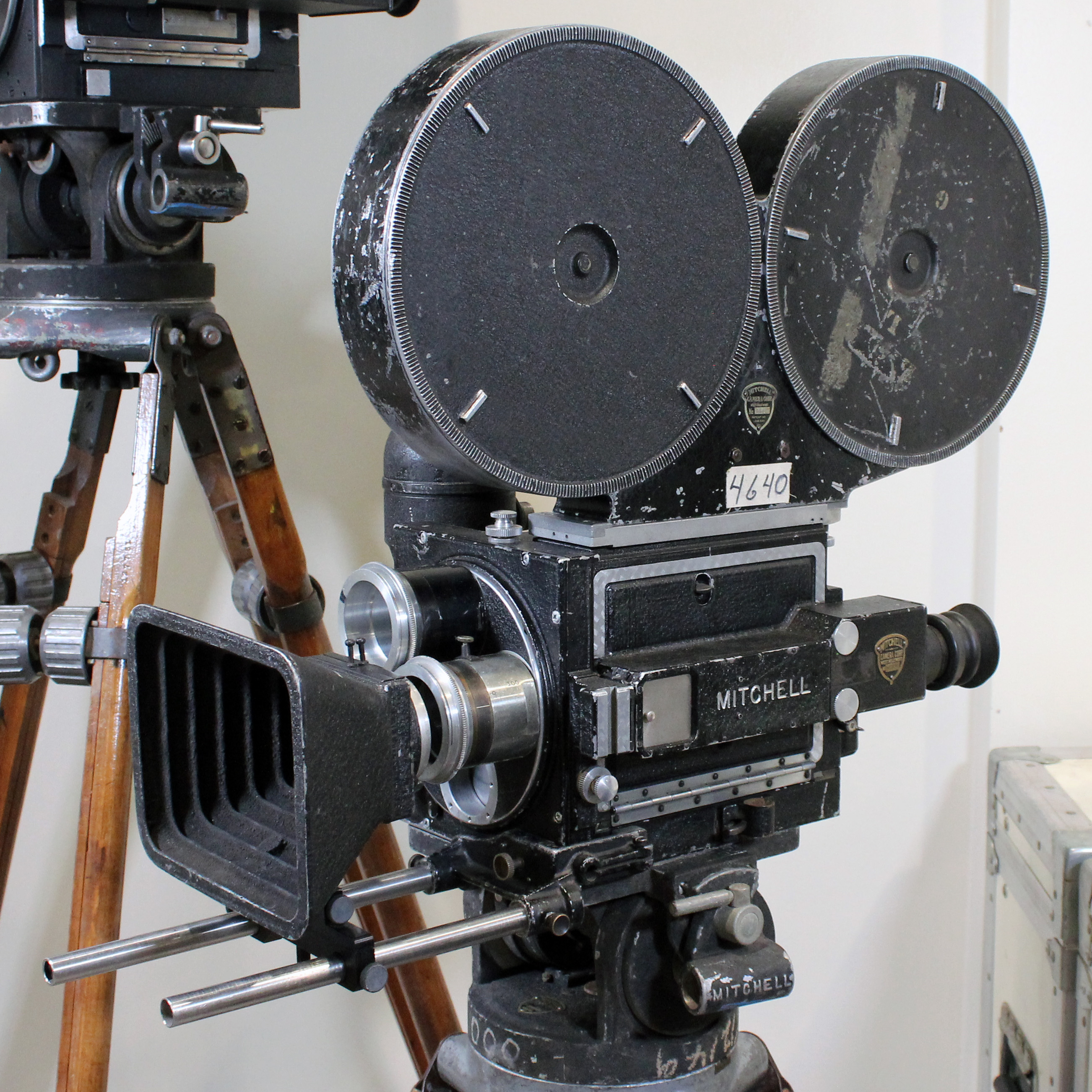 A Mitchell NC 35mm motion picture camera on a tripod with part of a second Mitchell camera in the background.